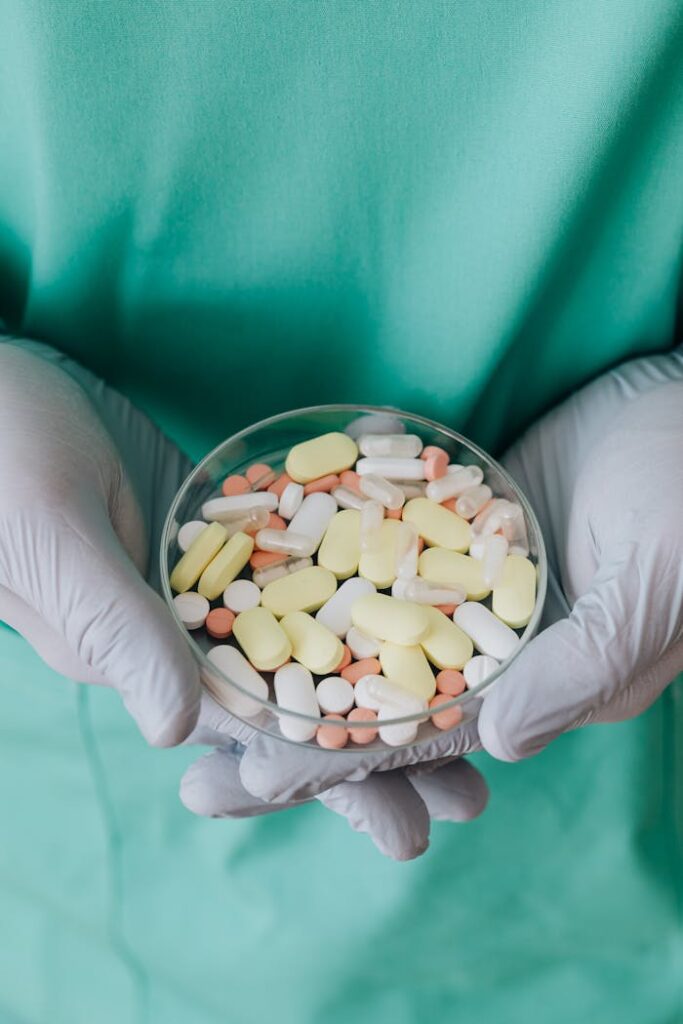pexels-photo-4021813 Gloved hands holding a bowl of mixed pills, representing pharmaceuticals.